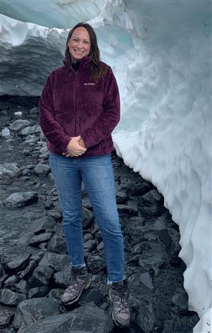 Ms. Ford stands next to a wall of snow with water running nearby